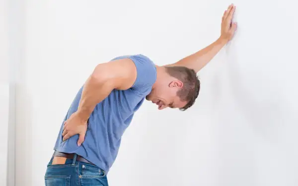 Uomo con mal di schiena appoggiato al muro, cerca rimedi naturali per il mal di schiena.